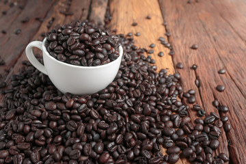 Close up shot of dark roasted coffee bean in white ceramic cup on wooden floor with copy space
