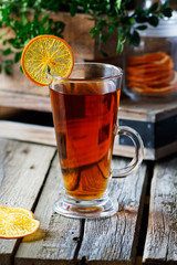High glass cup of black tea with a slice of dried orange on a bright wooden rustic background  and foliage.