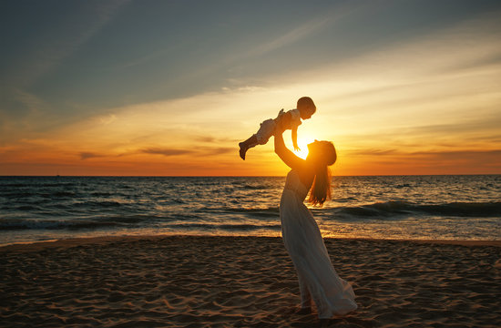 happy family mother with baby son walks by ocean on beach in summer
