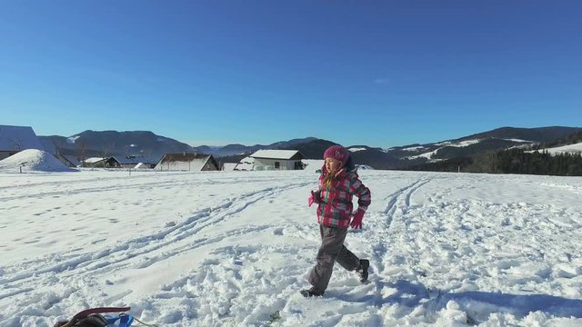 Small girl running and playing in snow in mountains on sunny day