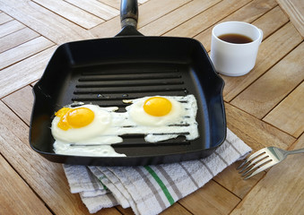 Two fried eggs on the pan and coffee on the wooden table