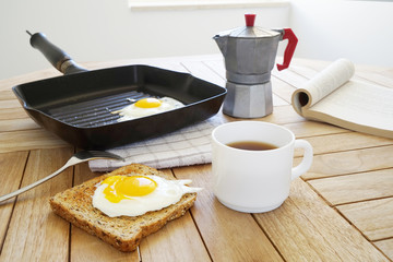 Fried eggs with toast, book and coffee on the wooden table