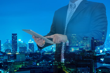 double exposure of business man using tablet with night modern city building background