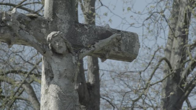 Old tombstone with Jesus cross on a sunny spring day. Pan from right to left on the cross. 4K in SLOG3. Medium shot.