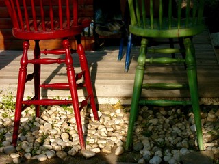 Bunte Barstühle in Rot und Grün aus Holz auf Kieselsteinen an einer Bar im Sommer bei...