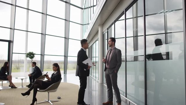  Businessmen talking as they walk through lobby of corporate office building
