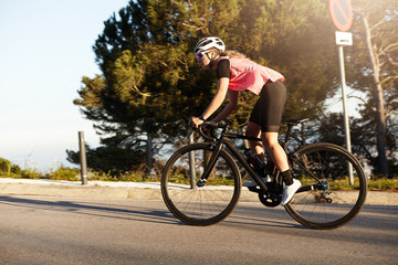 Side view of healthy athletic European woman cycling alone in helmet and sunglasses, riding bike at countryside, spending her active summer weekend, feeling free of exhausting urban life and rhythm