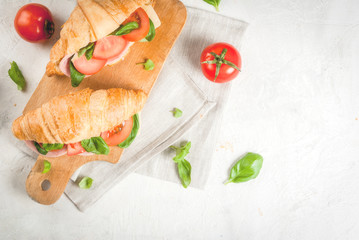 Light and hearty spring breakfast. Croissant with ham, cheese, fresh tomatoes and basil. On a white stone table, with the ingredients. Copy space top view