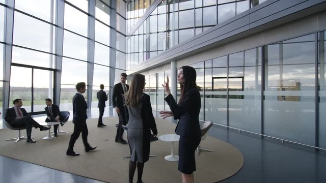  Businesswomen talking as they walk through modern glass office building