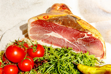 Italian prosciutto is on the counter with arugula and tomatoes.
