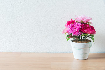 artificial flower pot on wooden table and white wall background