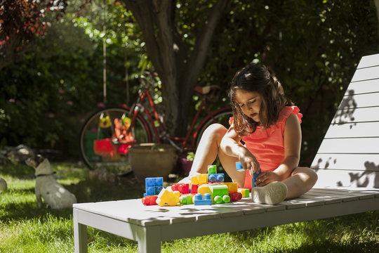 Portrait girl building with plastic construction toys in the garden. Spring