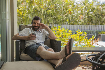 Relax smiling young man looking to the phone in the backyard