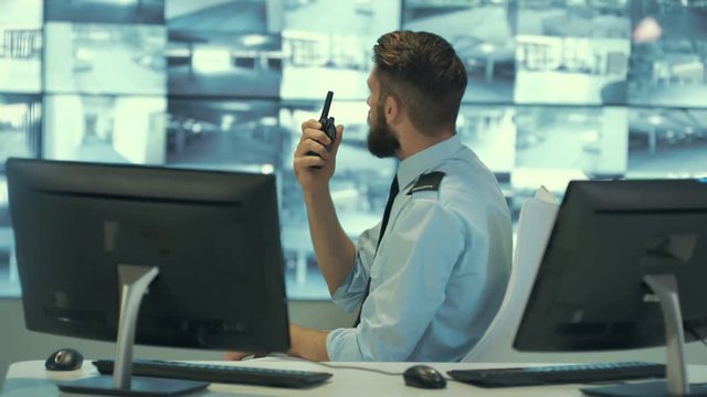  Security team watching CCTV video screens & communicating by radio in observation control room. 