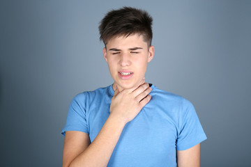 Sick young man having pain in throat on color background