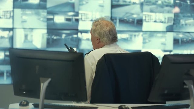  Security team watching CCTV video screens & communicating by radio in observation control room. 