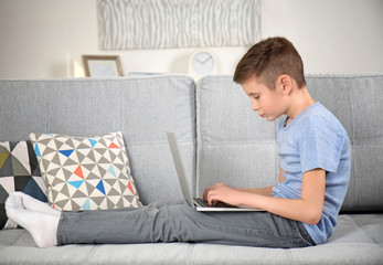 Incorrect posture concept. Schoolboy with laptop sitting on sofa