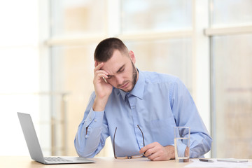 Fototapeta na wymiar Handsome young man suffering from headache while working in office