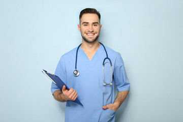 Young medical assistant with clipboard on color background