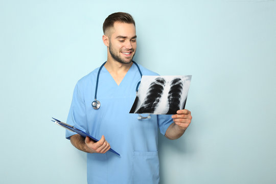 Young medical assistant with x-ray image and clipboard on color background
