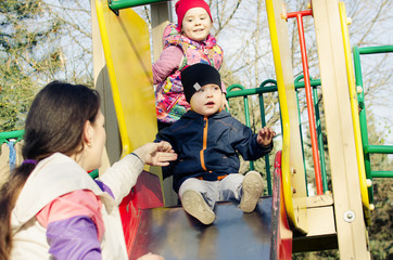 A brother with his sister and mother slides down the hill on the playground