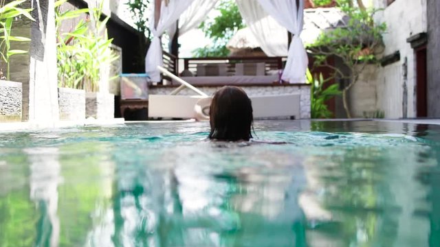 Attractive young caucasian female enjoying leisure time in her swimming pool on a luxury villa, tropical island Bali, Indonesia. Slow motion.