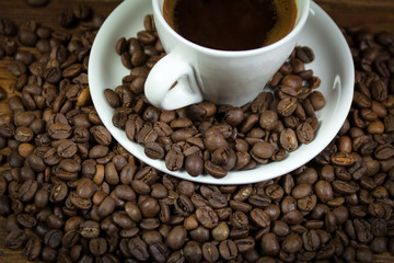 A cup full of coffee with coffee beans on a platter and wooden table
