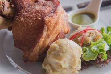 Pork knuckle with fried and mash potato on a white plate .