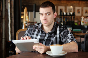 A successful young man in a dark plaid shirt in the cafe does business. Young hipster holding a smartphone, tablet computer. Office worker on lunch. business meeting. send a message.