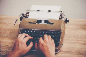 Hands typing on vintage typewriter on wooden table.