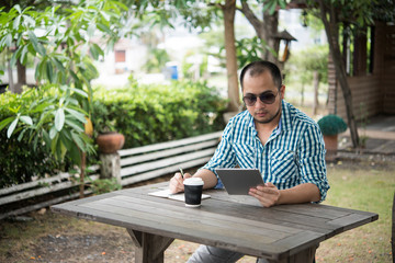 Fototapeta premium Businessman work on tablet and writing while sitting at wooden table at home.