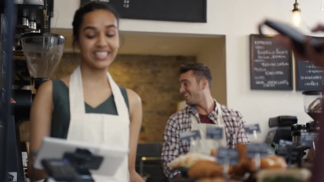  Cheerful Worker Serving A Customer Who Uses Smartphone To Pay In Coffee Shop.