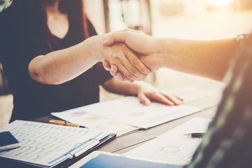 Close-up of two business people shaking hands while sitting at the working place.