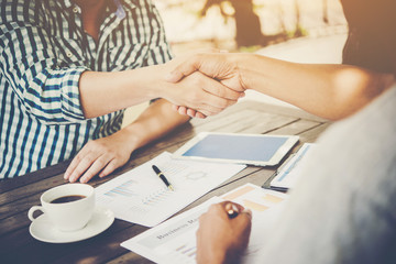 Close-up of two business people shaking hands while sitting at the working place.