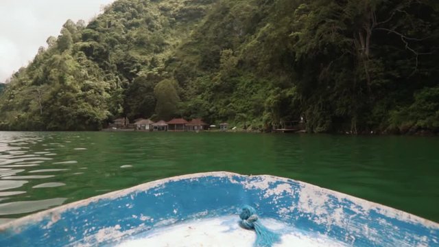 View from a small blue boat to Trunyan cemetery shore covered by trees and bushes on cloudy day. Shot with Sony a7s in Bali, Indonesia