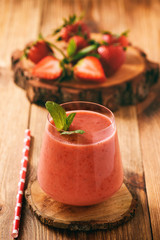 Strawberry smoothie in glass on wooden stump.