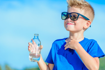 Portrait of a thirsty handsome boy in sunglasses drinking water on the desert tropical beach
