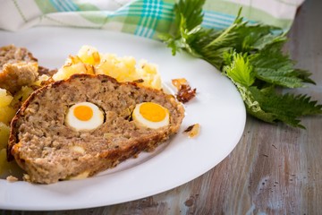 Portion of meatloaf on white plate with mashed potatoes and fresh nettle
