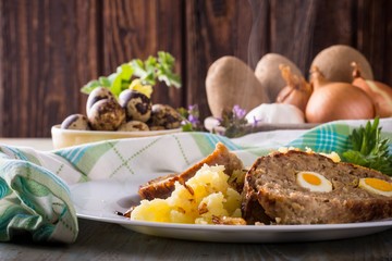 Portion of meatloaf on white plate with potatoes and quail eggs