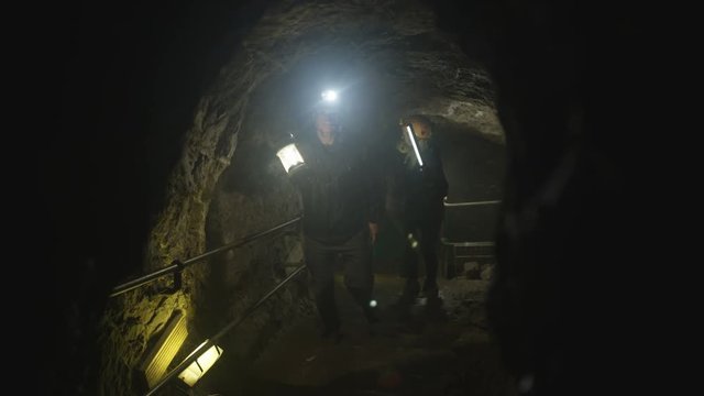 Team of potholers with hard hats and lamps exploring underground cave system