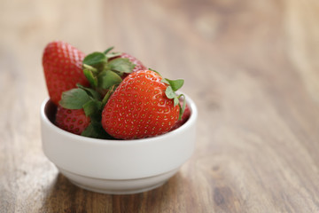 fresh ripe strawberries in white bowl on wood table, copy space