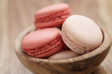 pastel colored macarons with strawberry and rose flavour in wood bowl on table