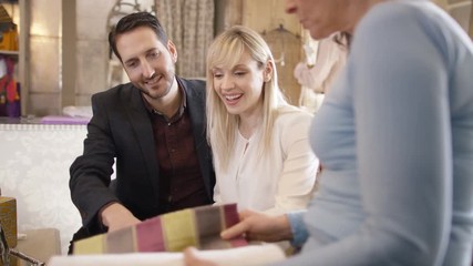  Couple with sales assistant, looking at fabrics in home furnishings store