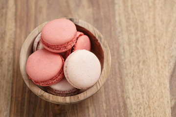 pastel colored macarons with strawberry and rose flavour in wood bowl on table