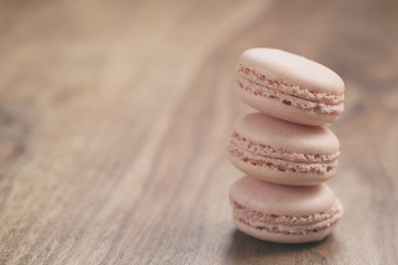 closeup shot stack of pastel colored macarons with rose flavour on wood table, vintage toned photo