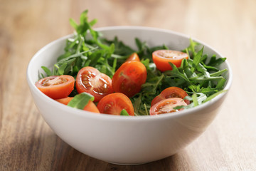 cherry tomatoes with arugula salad in white bowl on wooden table