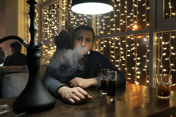 man smoking pipe of hookah in night cafe