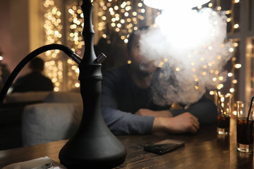man smoking pipe of hookah in night cafe