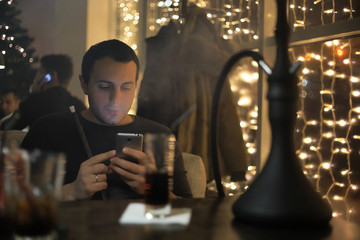 man smoking pipe of hookah in night cafe