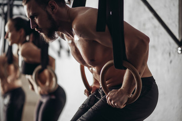 Group of young male and female adults doing pull ups on bar in cross fit training gym